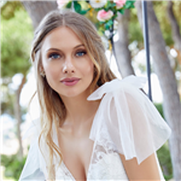 Close up of a blonde model in an ivory Ronald Joyce wedding dress with a sweetheart illusion neckline, matching long sheer sleeves and a tulle veil